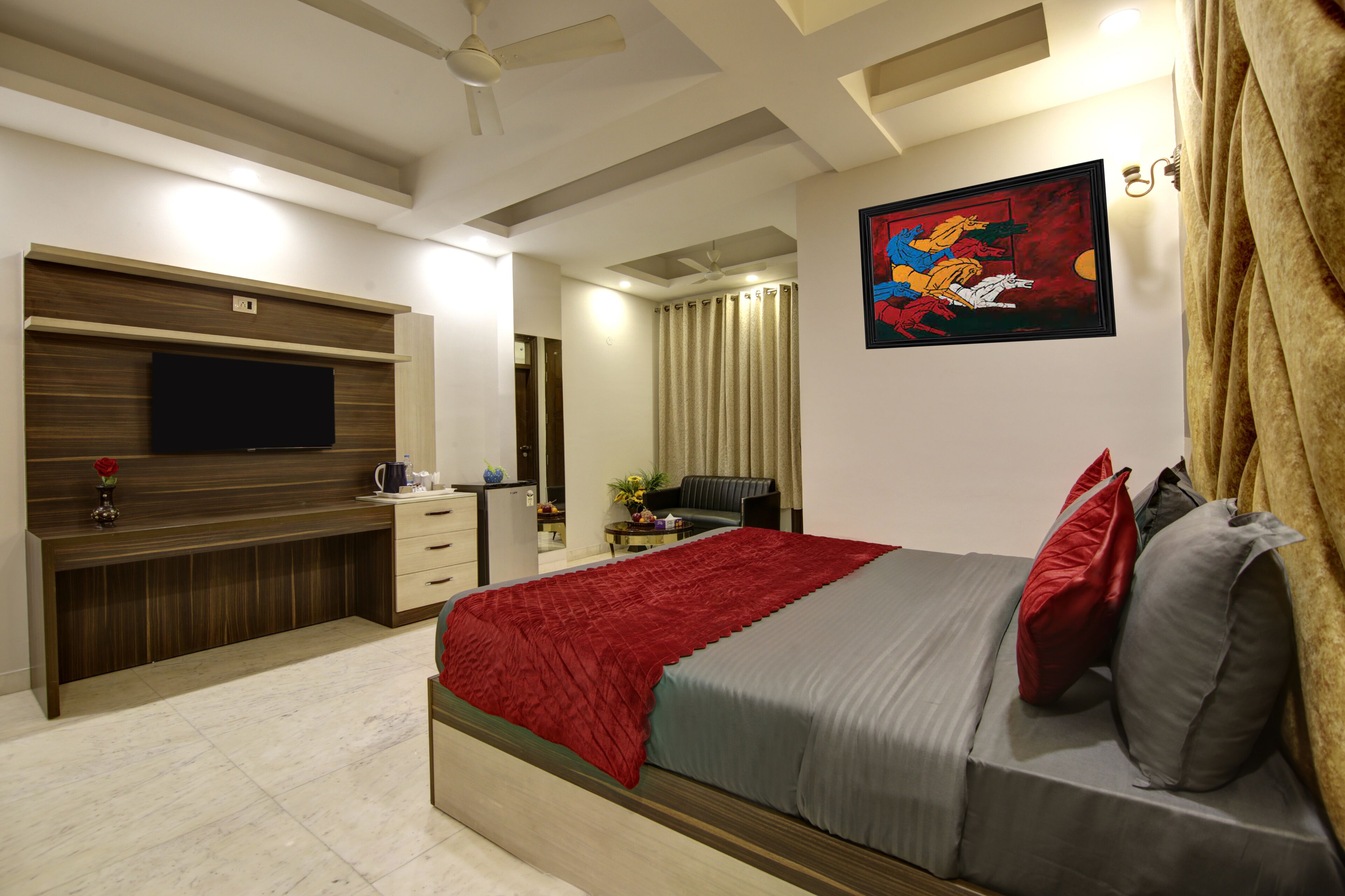 A modern bedroom with a bed, a TV, a desk, and a painting on the wall.