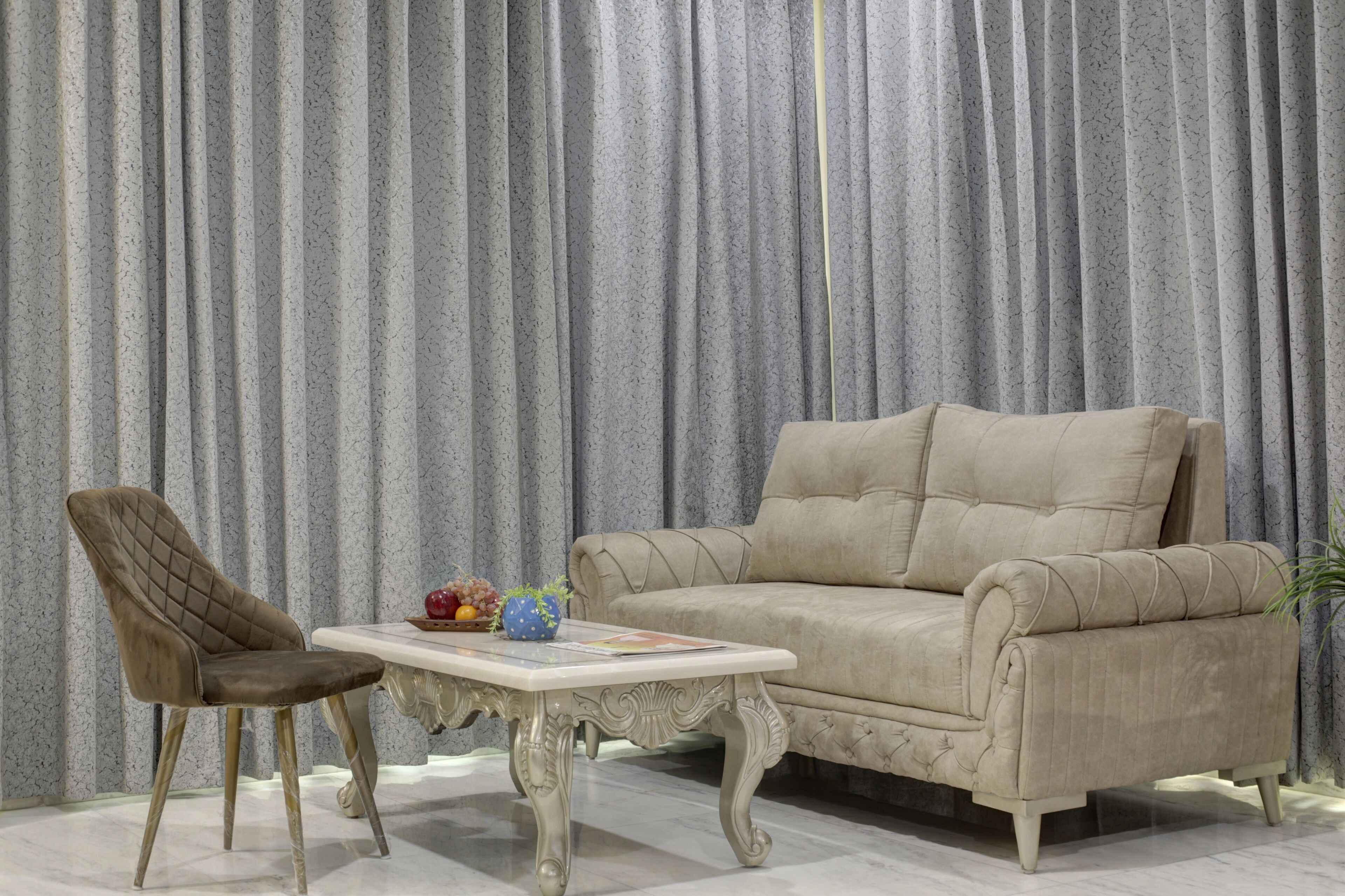 Un conjunto de sofá y sillón color beige frente a un fondo de cortina gris.