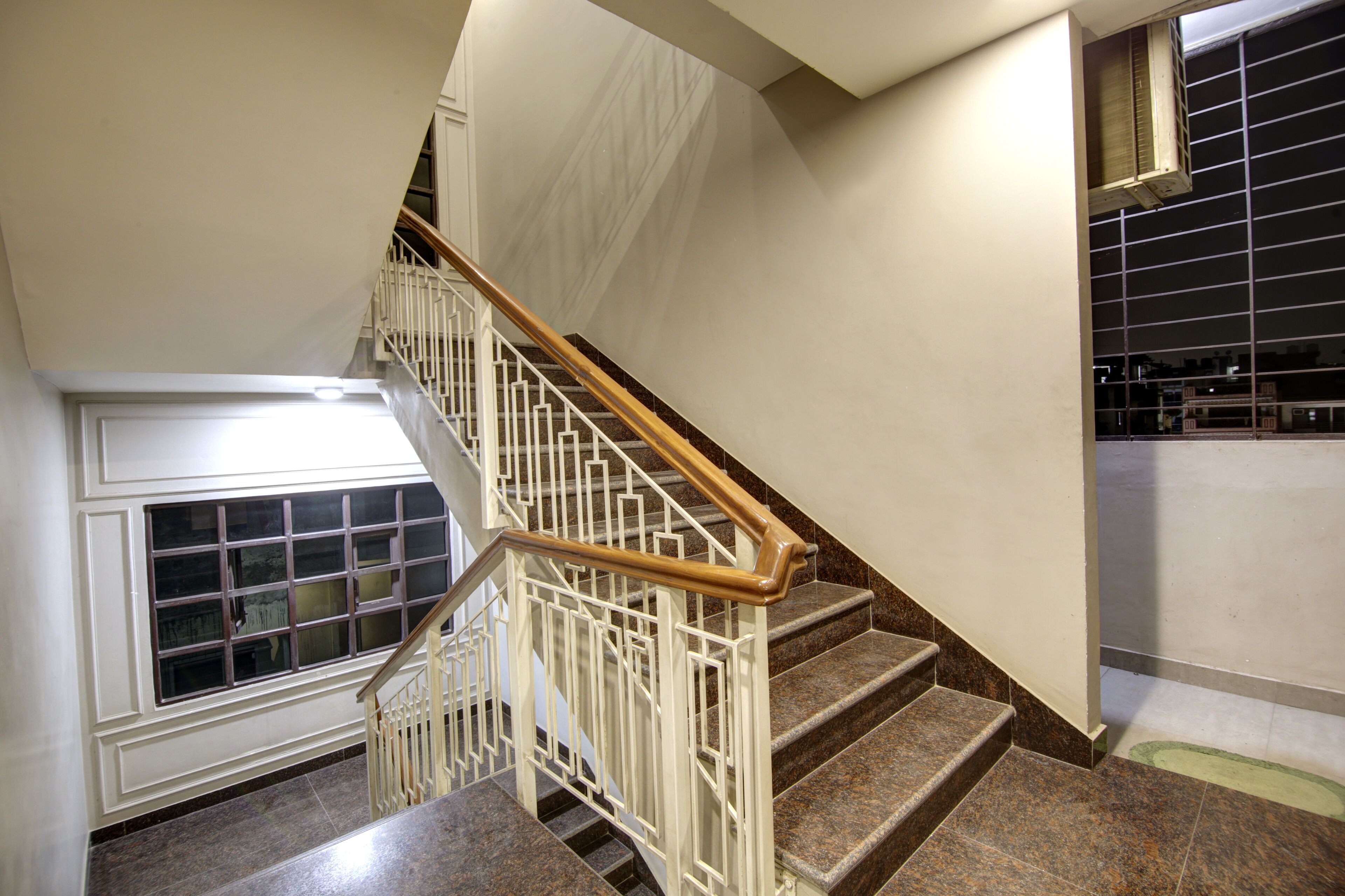 A staircase with a wooden handrail and white railings, leading to a landing with a window and a door.