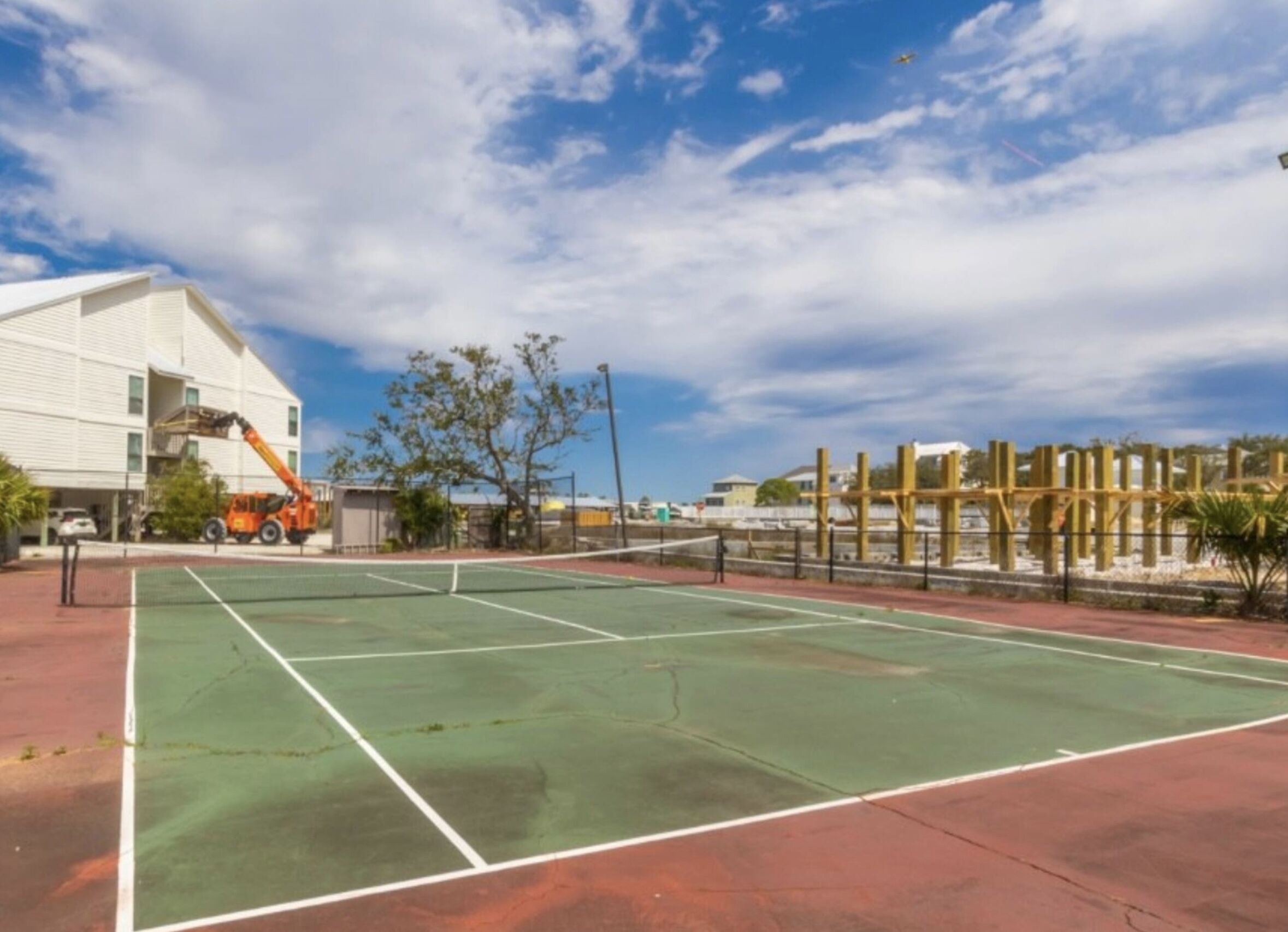 An outdoor tennis court with a net, surrounded by a fence and trees.