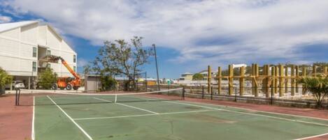 An outdoor tennis court with a net, surrounded by a fence and trees.