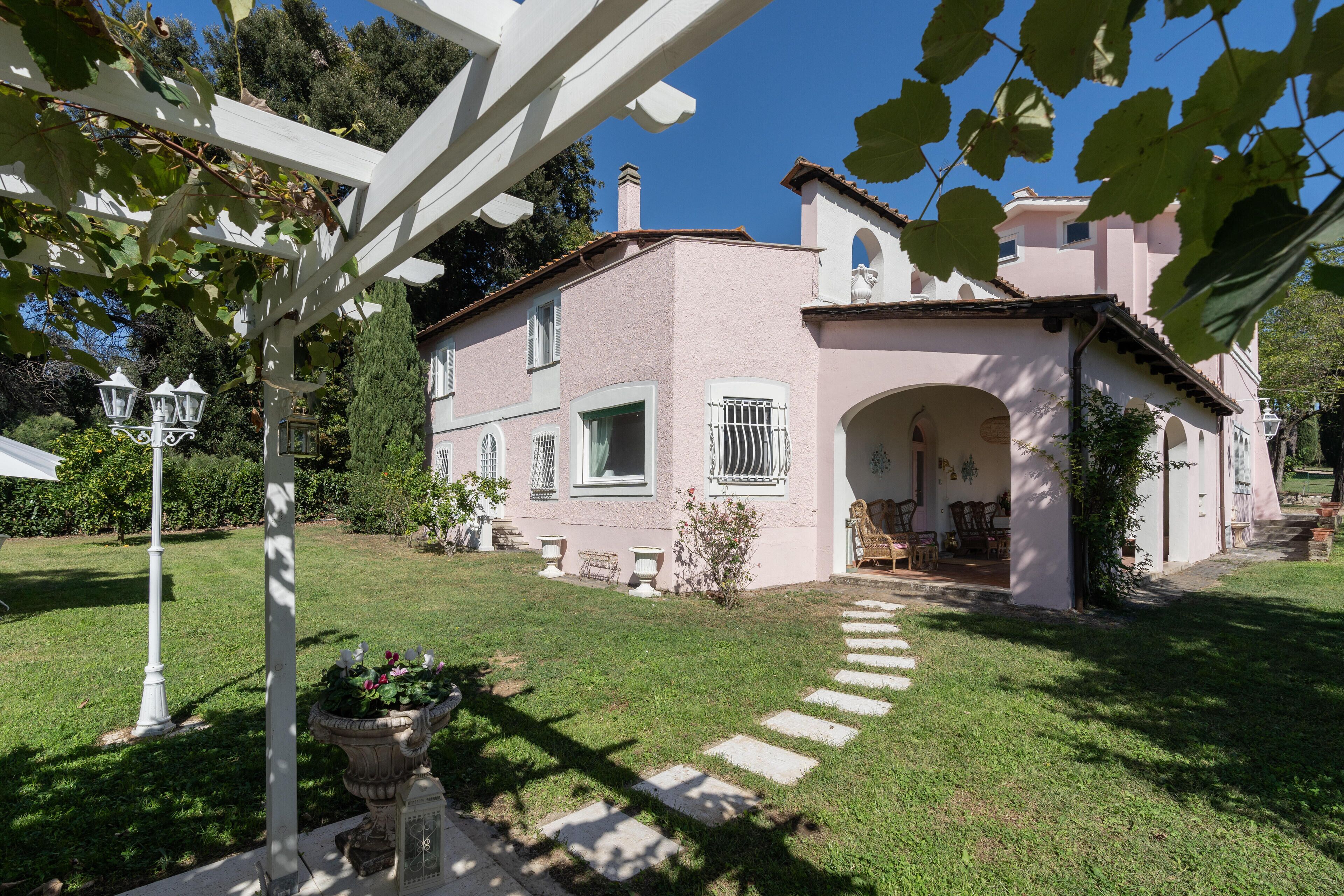 A pink house with a white porch, a garden with a pathway, and a white pergola.