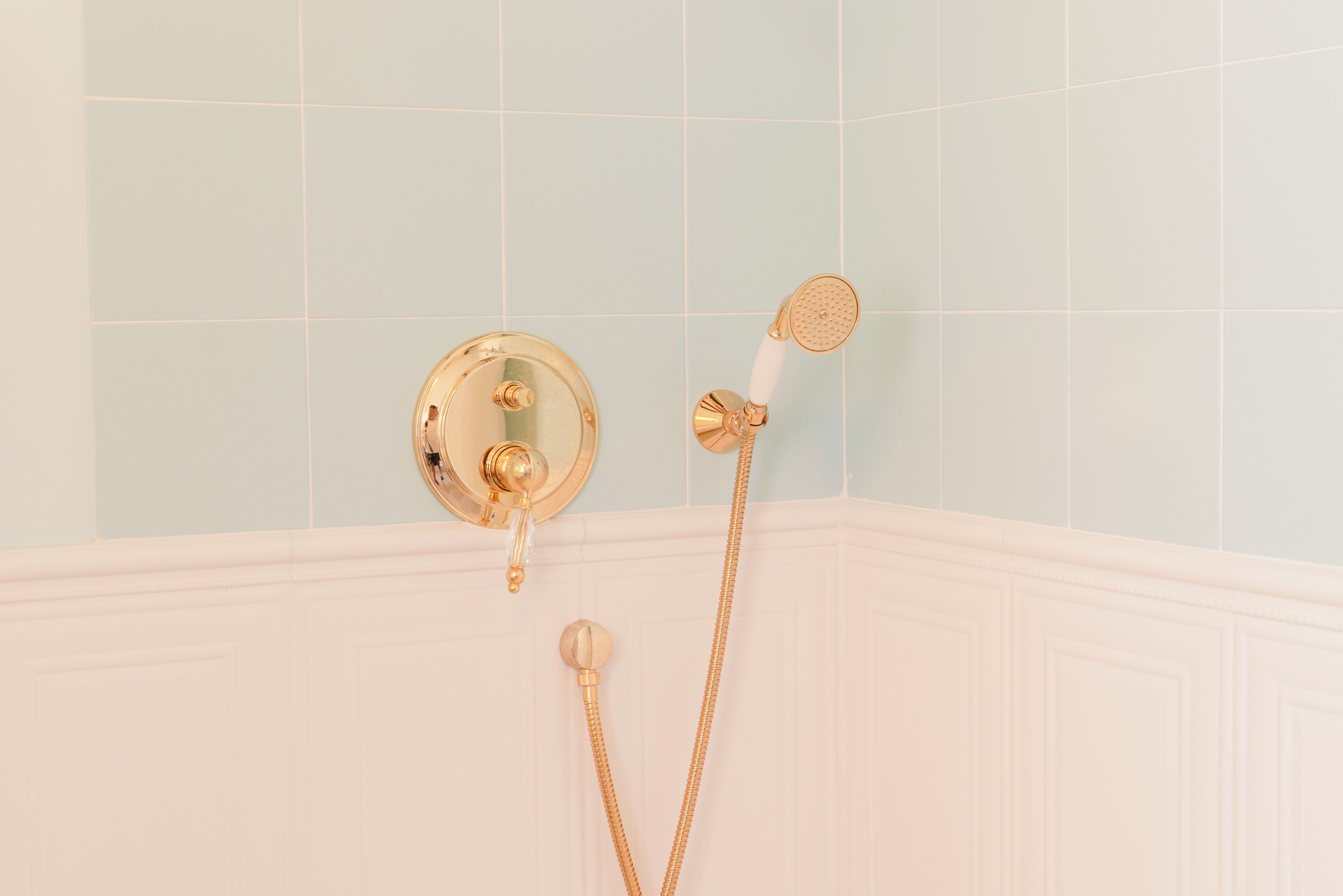 Un baño con cabezal de ducha dorado y mandos montados en una pared de azulejos azul claro.