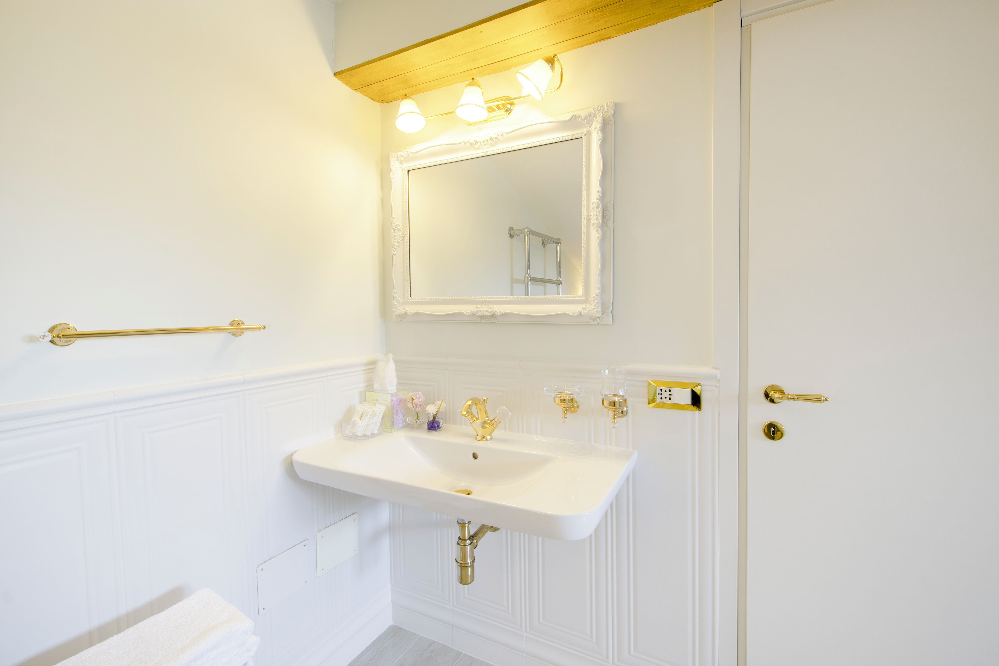 A bathroom with a white sink, gold fixtures, and a mirror with lights above.