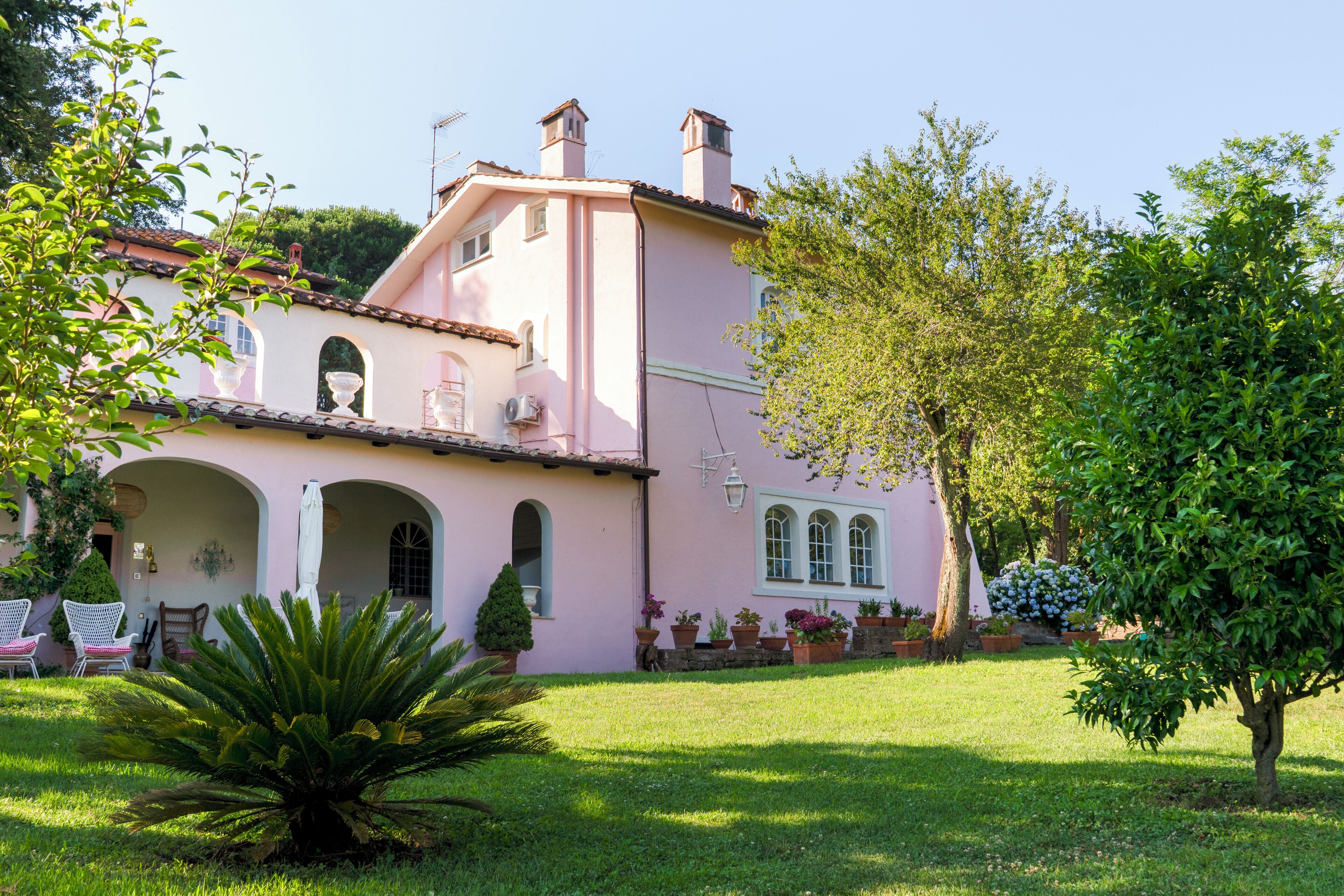 A pink villa with a garden, arched windows, and a tree in the foreground.