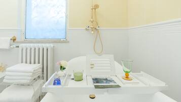 Un baño con una bañera blanca, un vaso de líquido verde, un libro titulado 'Leo Tolstoy' y una ventana con vistas al cielo.