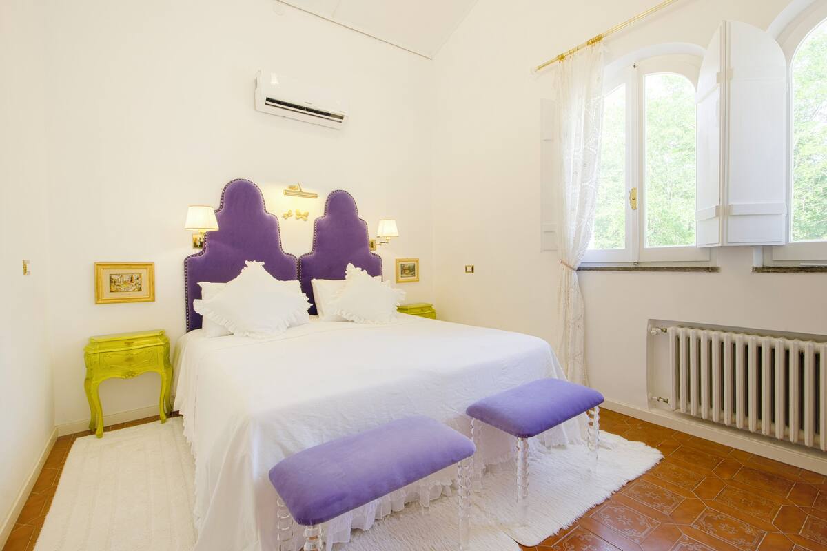 Een slaapkamer met een groot bed, twee nachtkastjes, een raam met gordijnen en een radiator.