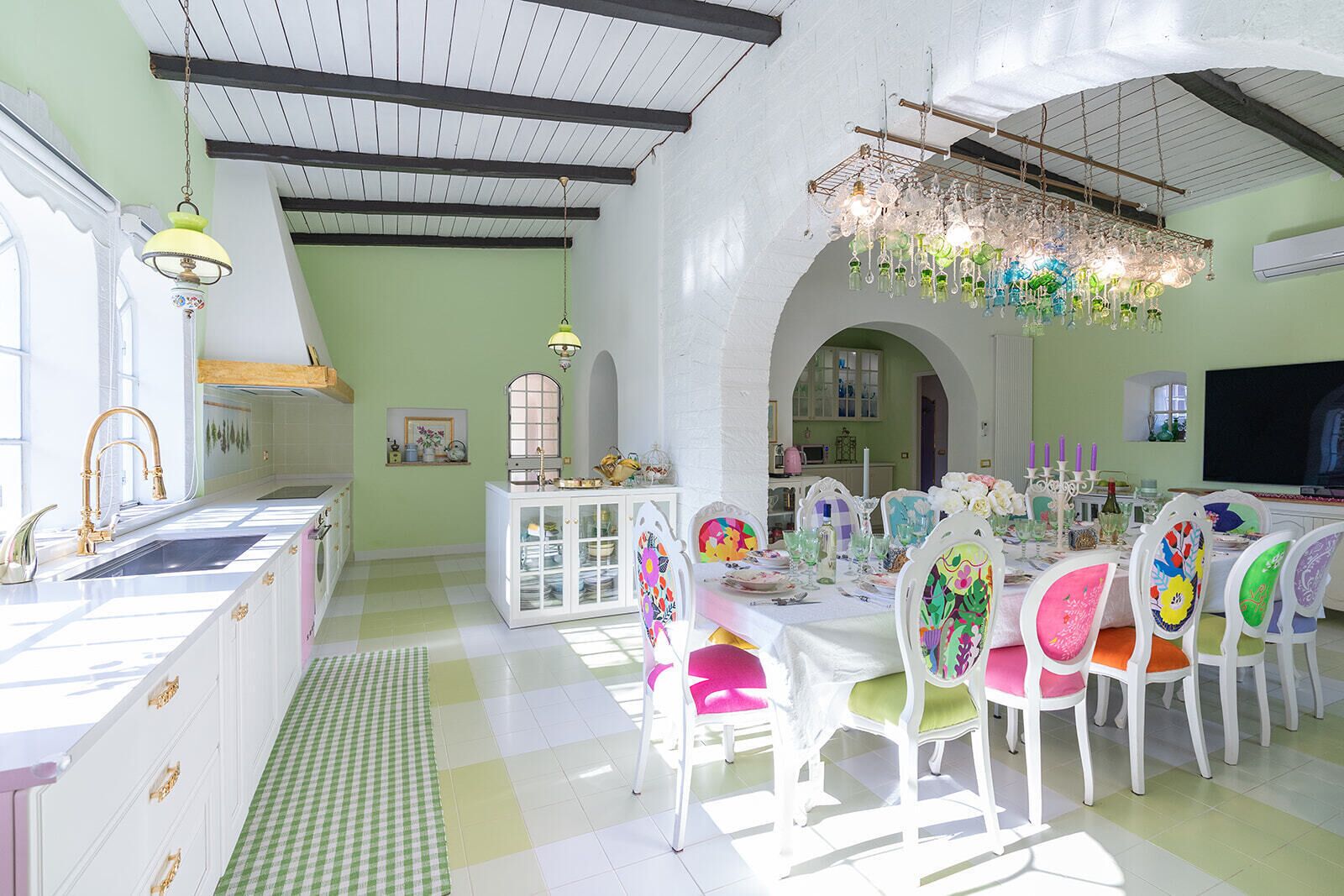Un comedor luminoso con mobiliario blanco, una araña y suelo a cuadros.