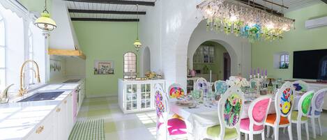 Un comedor luminoso con mobiliario blanco, una araña y suelo a cuadros.