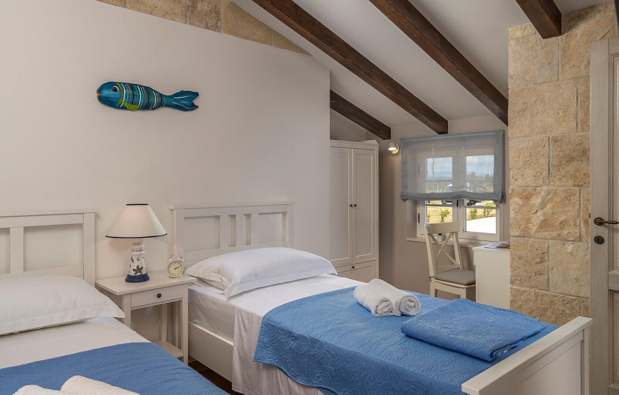 Camera d'albergo con due letti, televisore, orologio e un pesce decorativo appeso al muro.