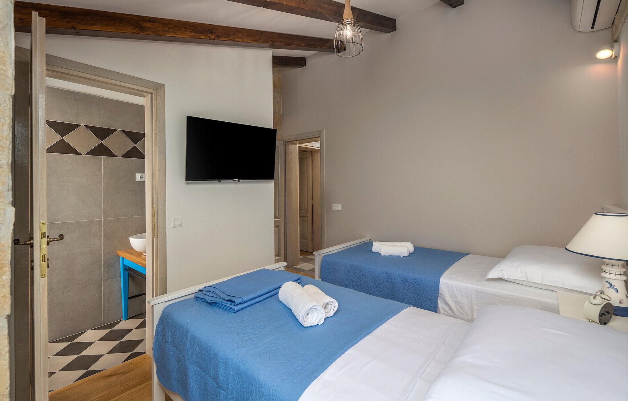 Habitación de hotel con dos camas, televisión, espejo y lámpara de noche.