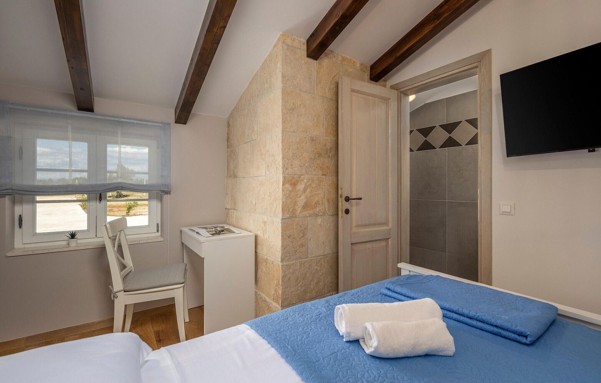 Ein Schlafzimmer mit Bett, Stuhl, Schreibtisch, Fenster und Tür.