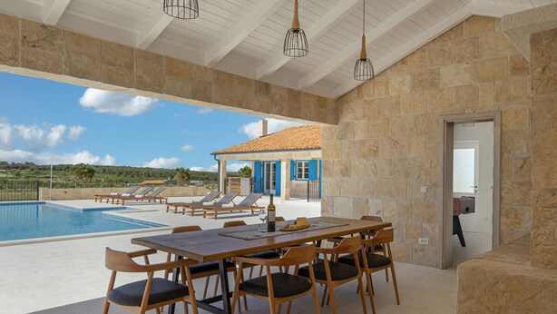 A poolside area with a table and chairs, a view of a house, and a clear sky. - Charming villa Viliska with heated pool (Sveti Filip i Jakov)