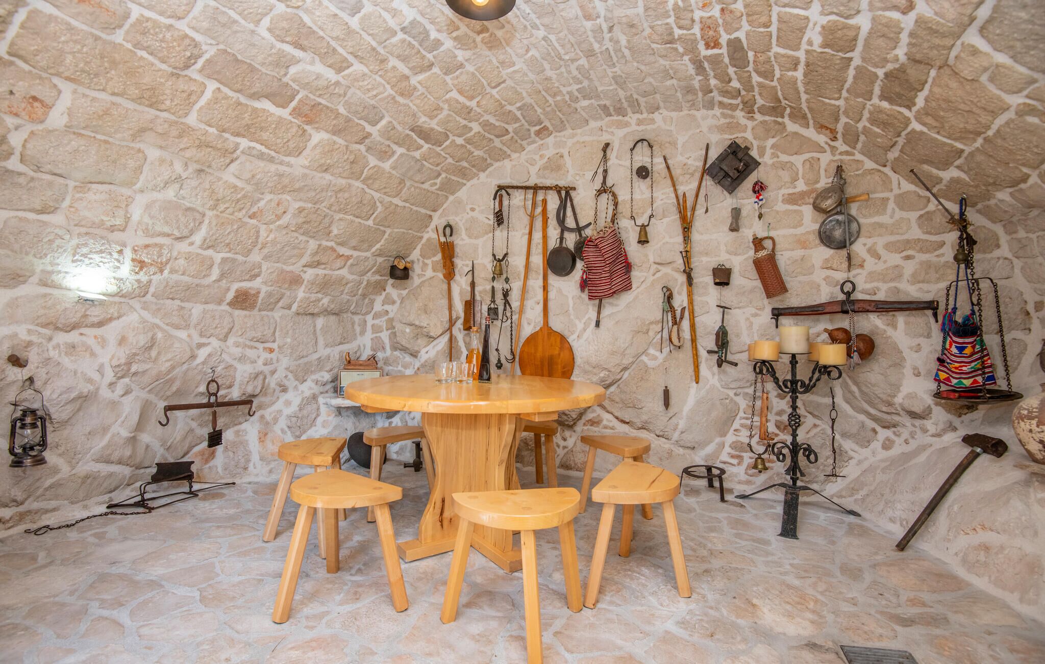 A stone-walled room with a round wooden table and six stools.