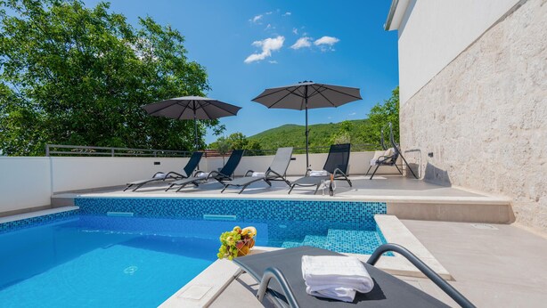 A pool area with lounge chairs and umbrellas, a tiled pool, and a view of greenery and hills. - Nice home in Dobrince (Dobrince)