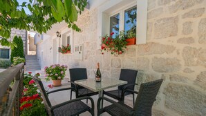 A stone building with a small outdoor seating area featuring wicker chairs and a table with a bottle of champagne. - Nice home in Dobrince (Dobrince)