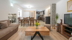 A modern living room with a sofa, coffee table, TV, and a dining area with chairs and a table. - Nice home in Dobrince (Dobrince)