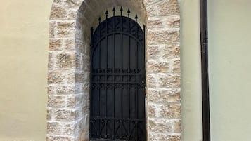 Un arc en pierre mène à une porte en métal noir, précédée d’un petit escalier.