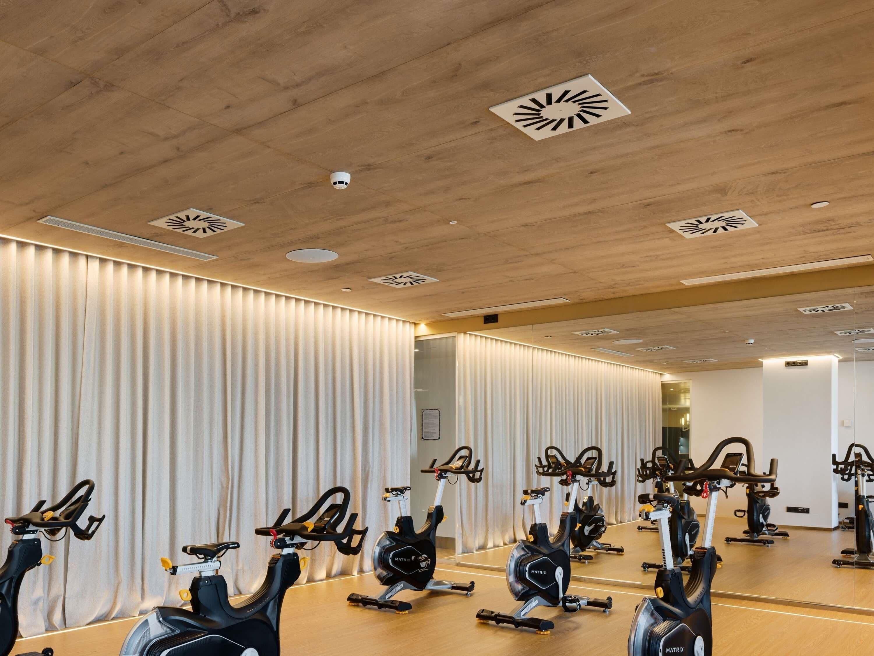 A gym with multiple stationary bikes, wooden ceiling, and mirrored walls.