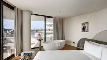 Habitación de hotel moderna con una cama grande, una bañera y un balcón con vistas a la ciudad.