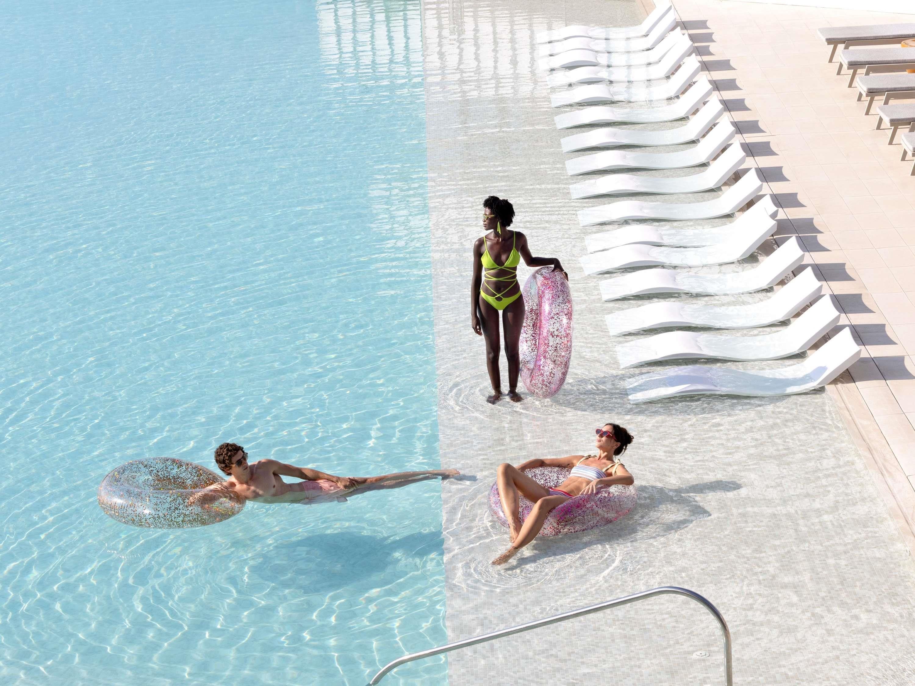 A swimming pool with lounge chairs and a person holding a floatation device.