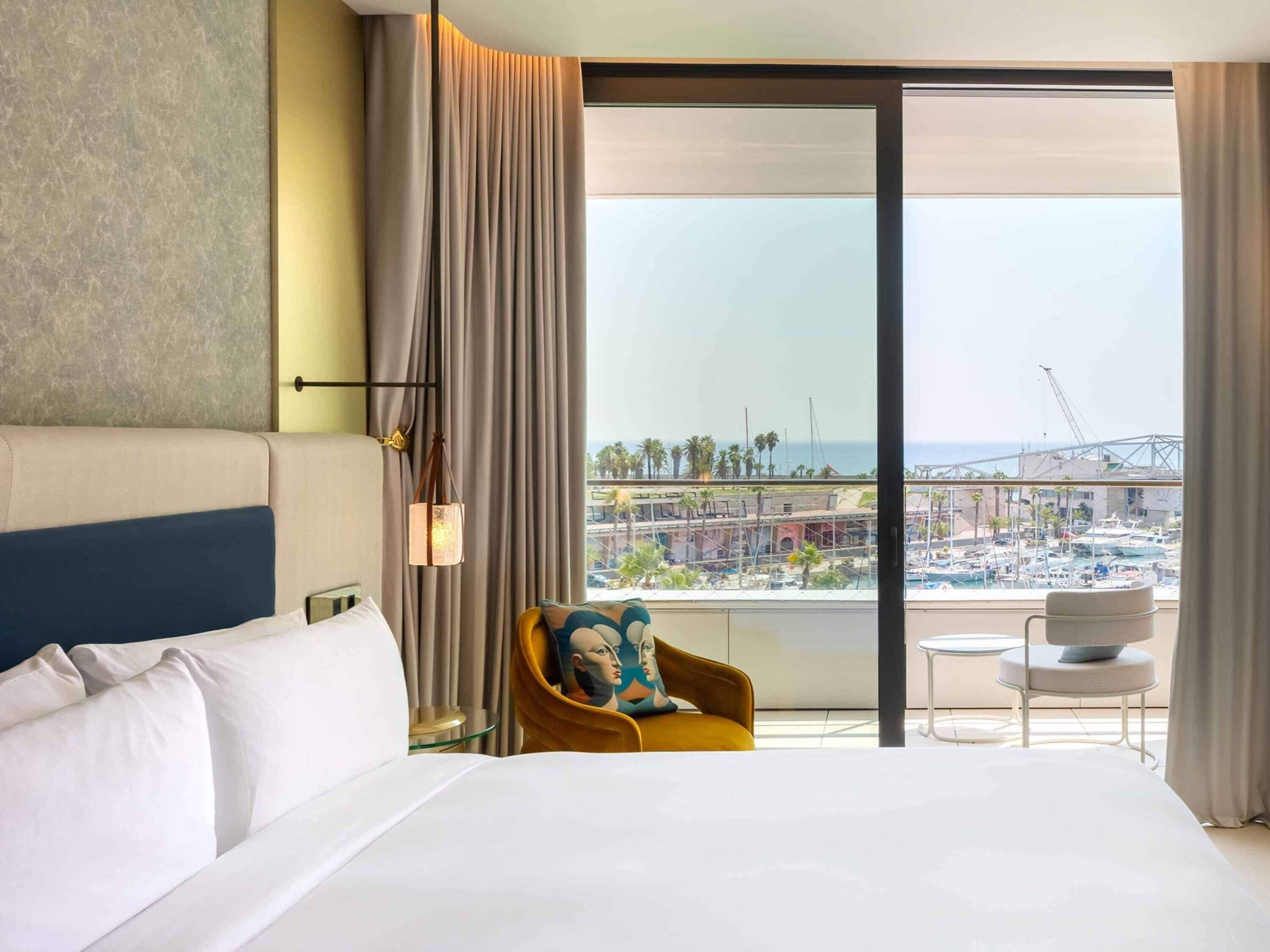 Ein Hotelzimmer mit einem großen Bett, einem Sessel, einem kleinen Tisch und Blick auf einen Hafen sowie Gebäude.