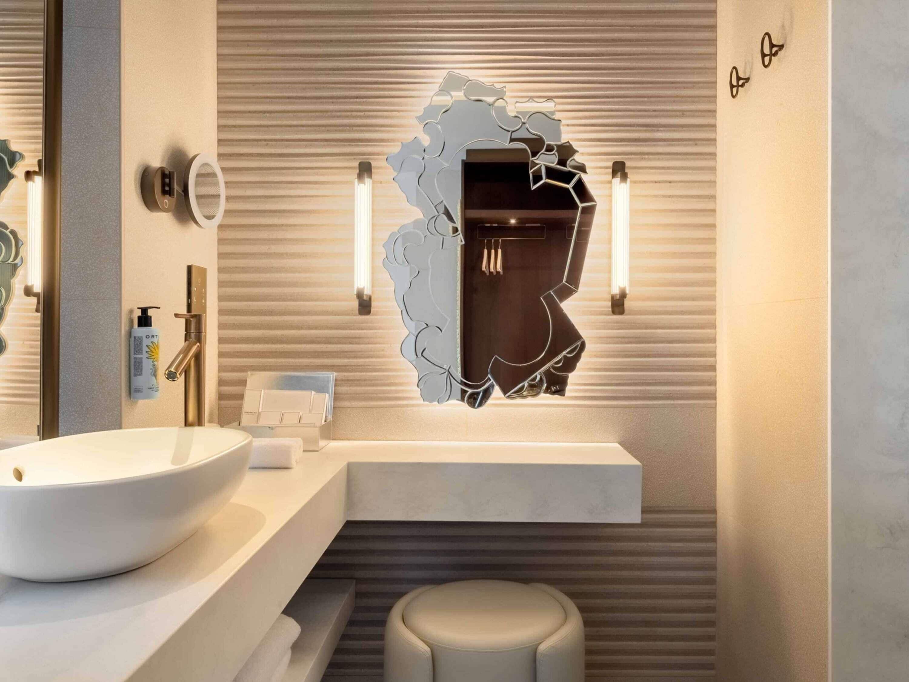 A modern bathroom with a large white sink, a mirror with a unique design, and a towel rack.