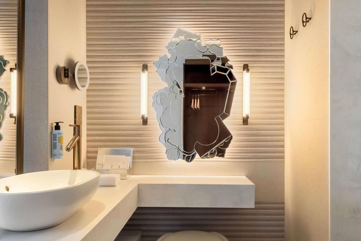 A modern bathroom with a large white sink, a mirror with a unique design, and a towel rack.