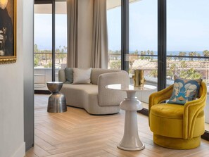 A modern living room with a sofa, a yellow armchair, a round table, and a large window offering a view of the beach. - SLS Barcelona (Sant Adria de Besos)