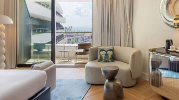 Habitación de hotel con cama, sofá, mesa de centro y vistas a un edificio y palmeras.