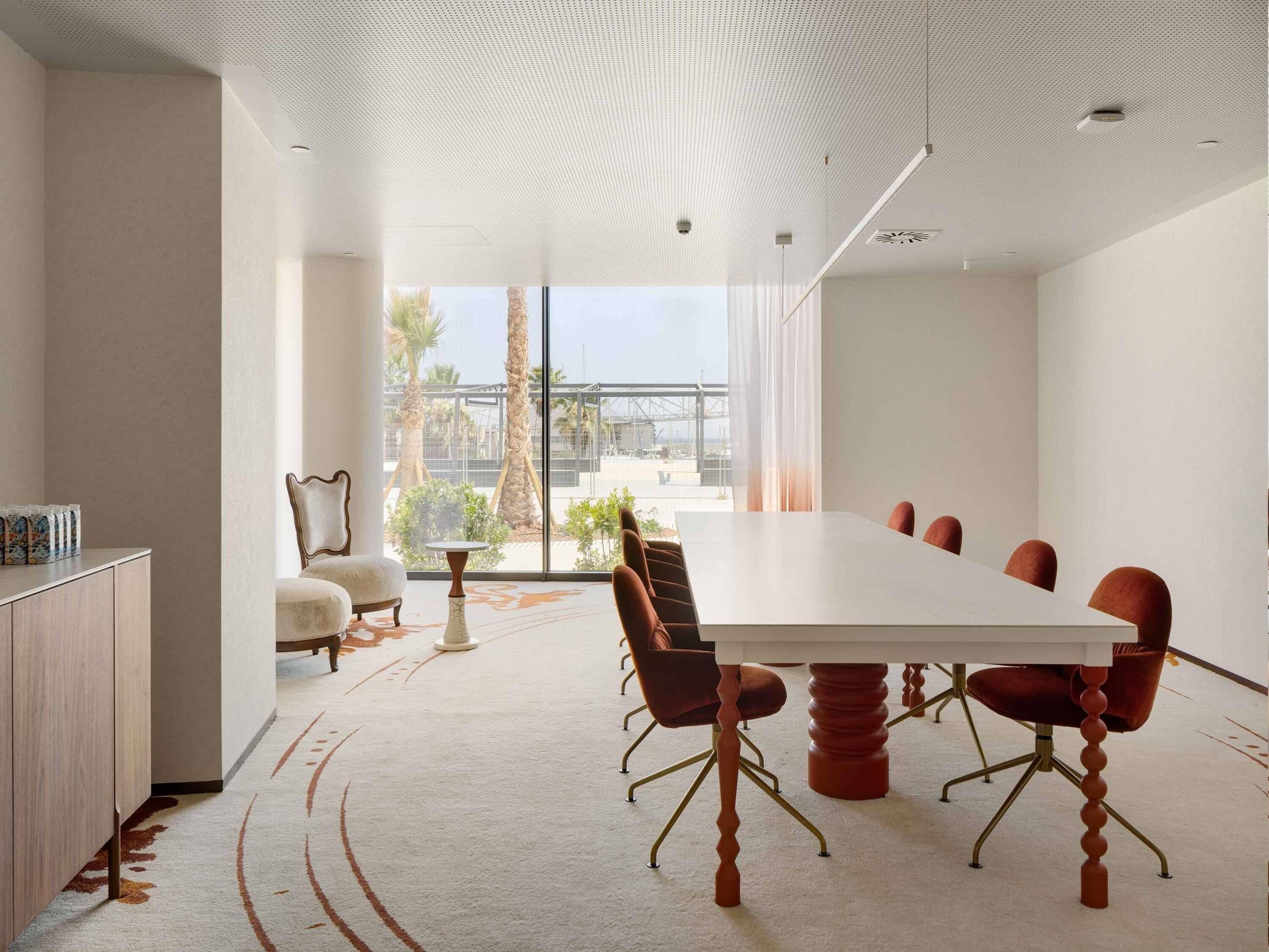 A conference room with a large table, chairs, a cabinet, and a view of palm trees and a bridge.