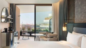 Een moderne hotelkamer met een groot bed, een zithoek met een tafel, een koffiehoek en een balkon met uitzicht op gebouwen.
