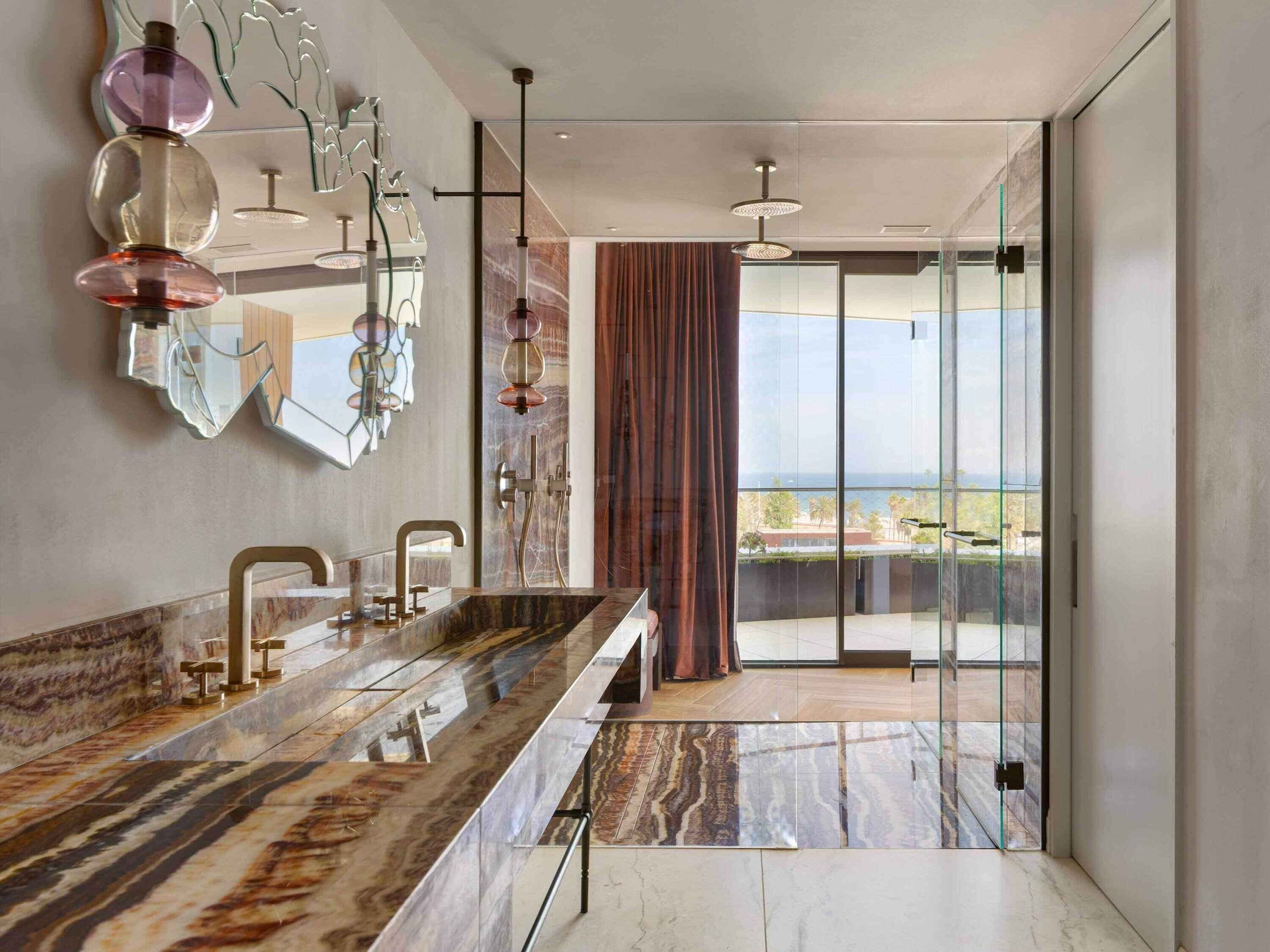 A modern bathroom with a marble vanity, glass shower enclosure, and a view of the sea.