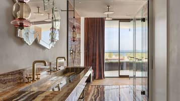 Un baño moderno con tocador de mármol, cabina de ducha de vidrio y vista al mar.