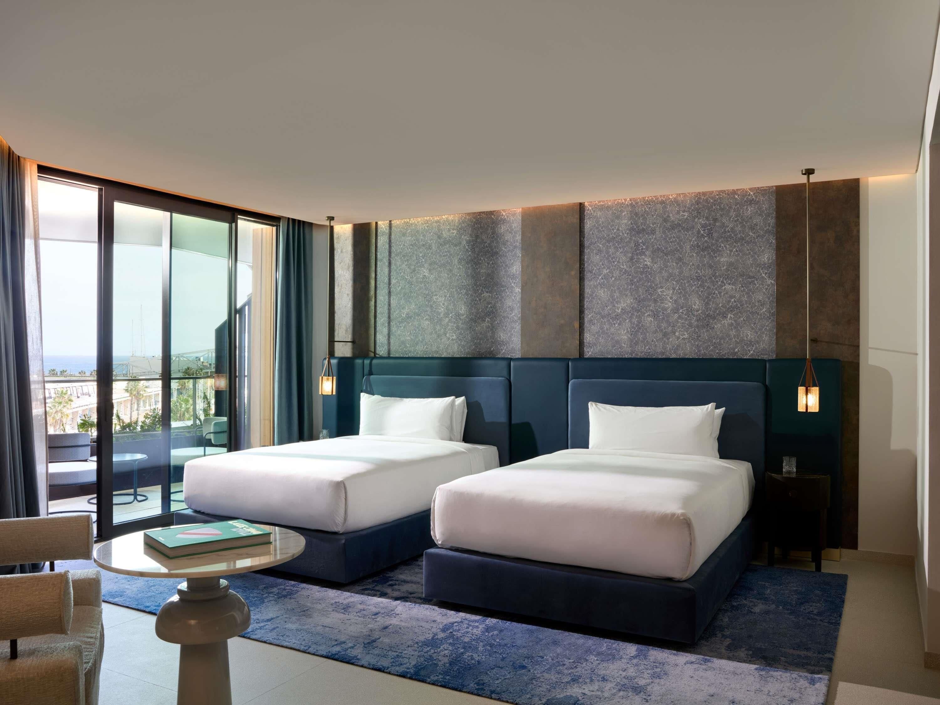 Una habitación de hotel moderna con dos camas, un balcón y vista al mar.