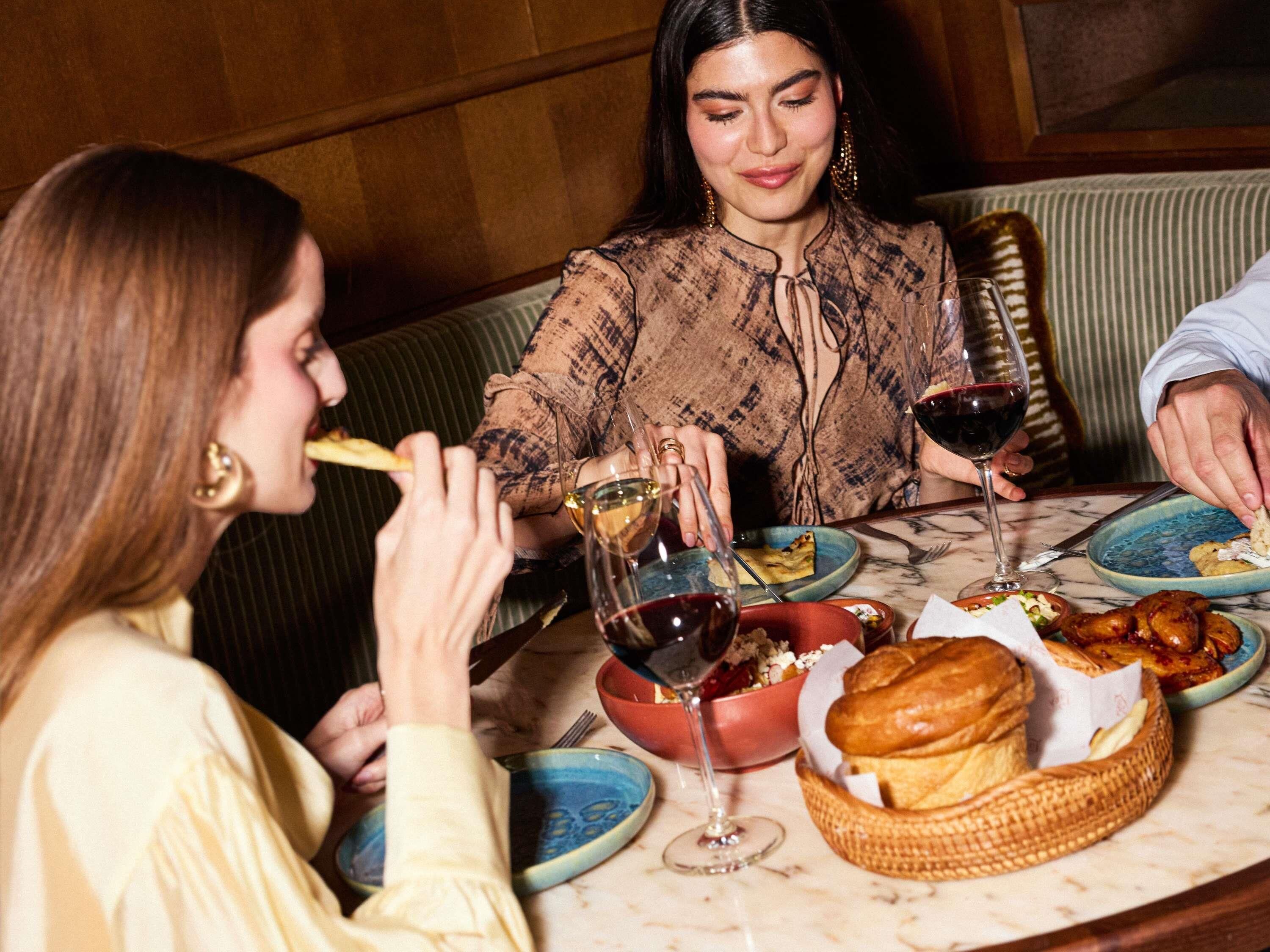 A group of people dining at a table with various dishes, glasses of wine, and a basket of bread.