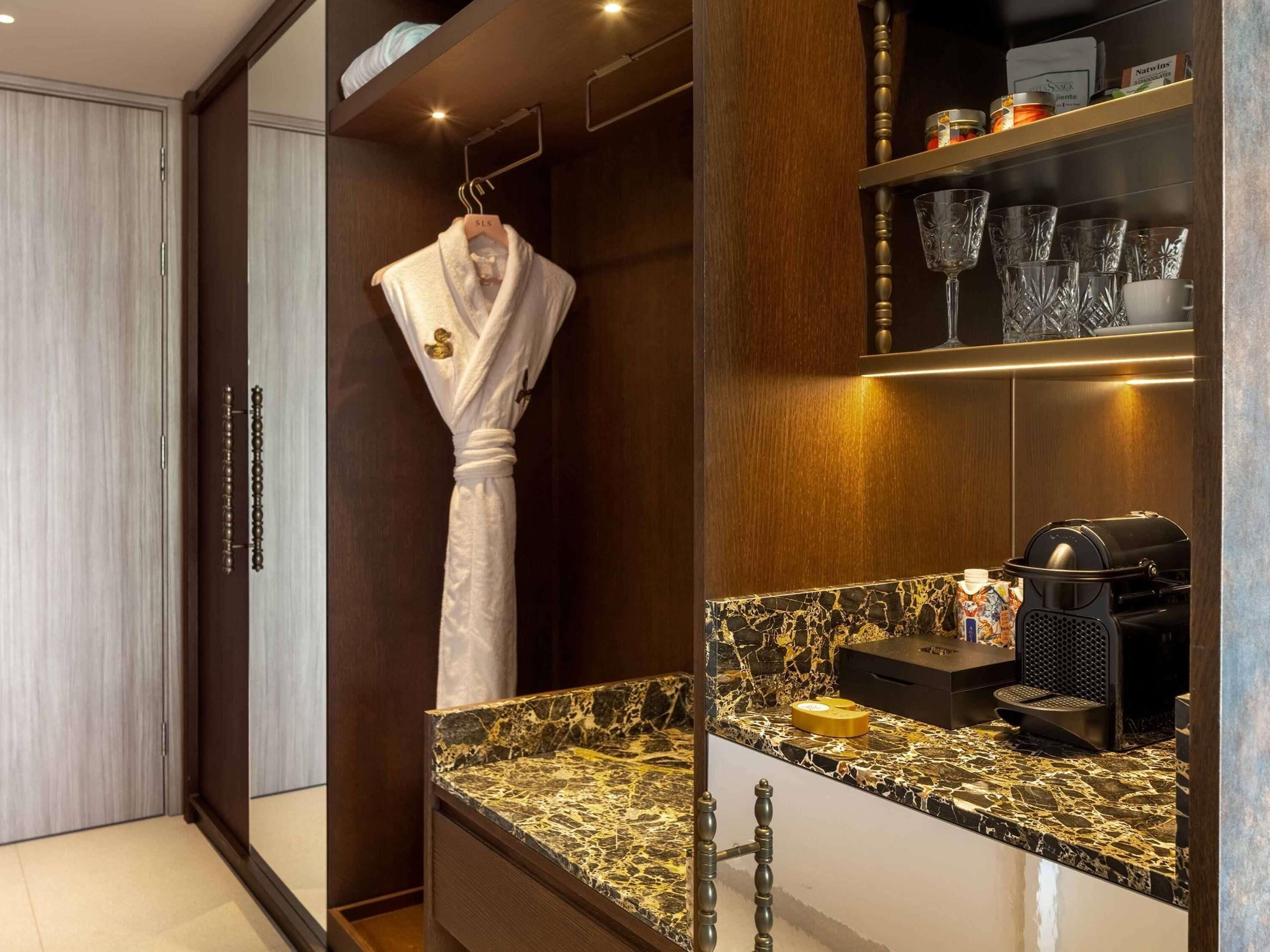 Un baño moderno con encimera de mármol, una bata colgada en un perchero y una máquina de café.
