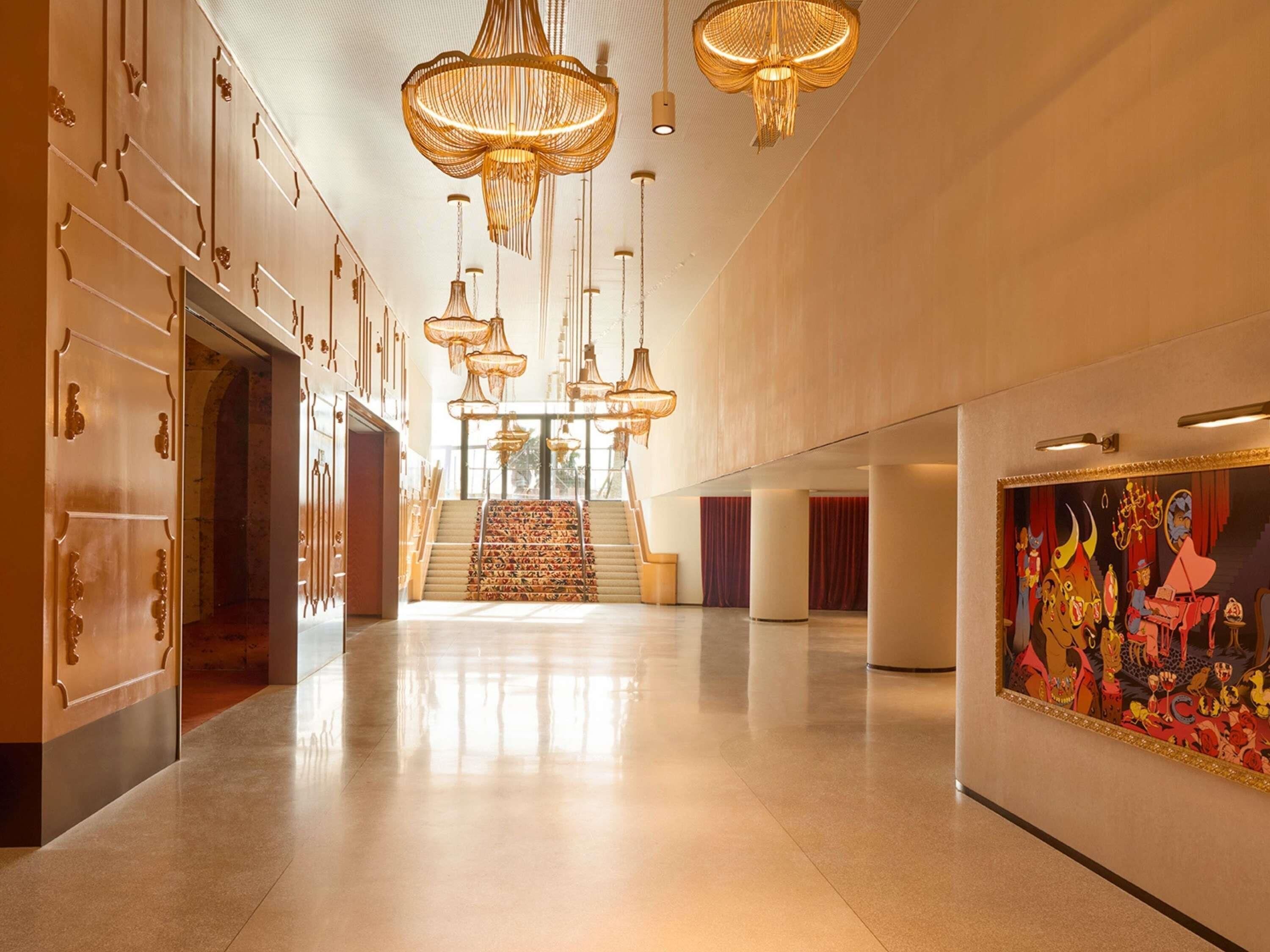 A spacious hallway with a grand staircase, ornate doors, and a large wall painting.