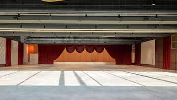 Um amplo auditório vazio com palco, cortinas vermelhas e um design de teto moderno.