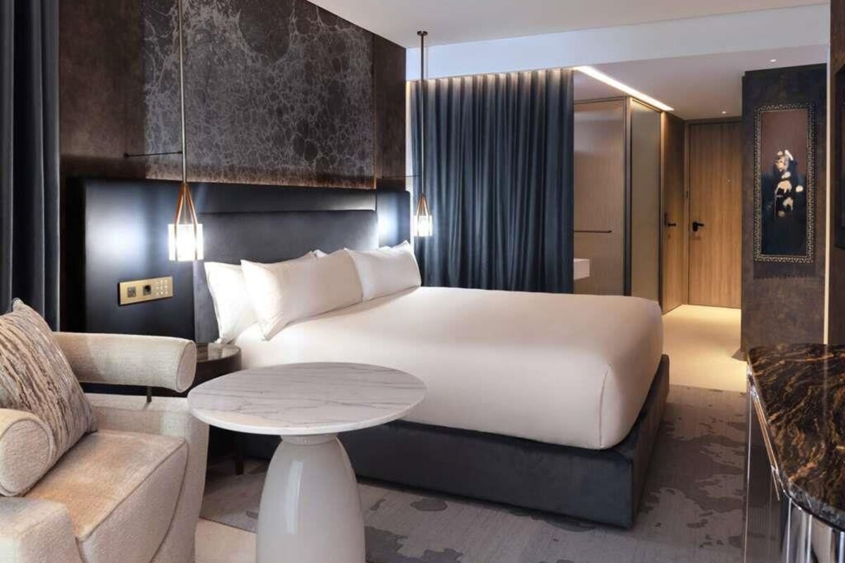 A modern hotel room with a large bed, a sofa, a round coffee table, and a dark accent wall.
