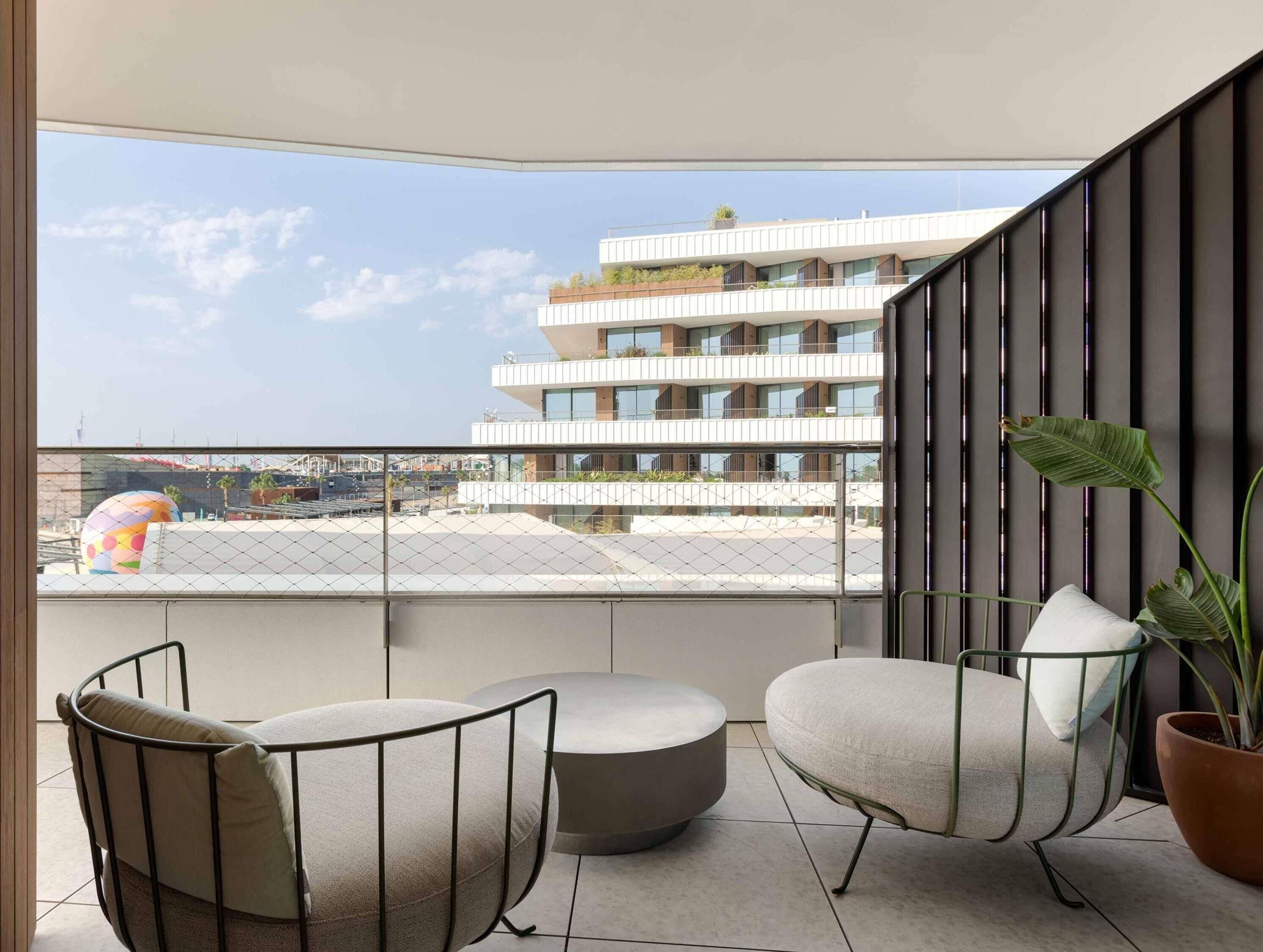 A balcony with two chairs, a potted plant, and a view of a modern building.
