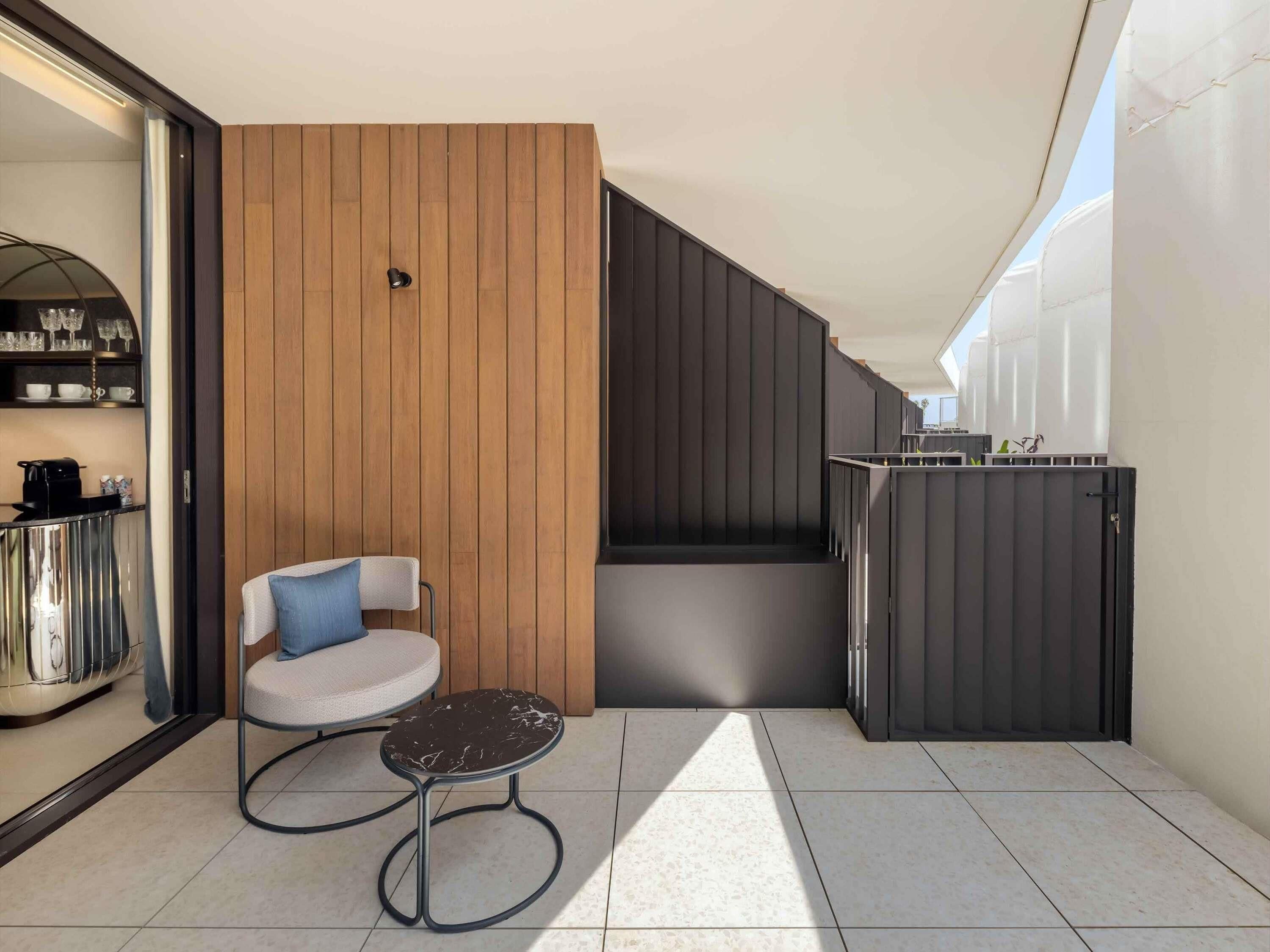 A modern balcony with a wooden panel wall, a round table with a chair, and a metal railing.