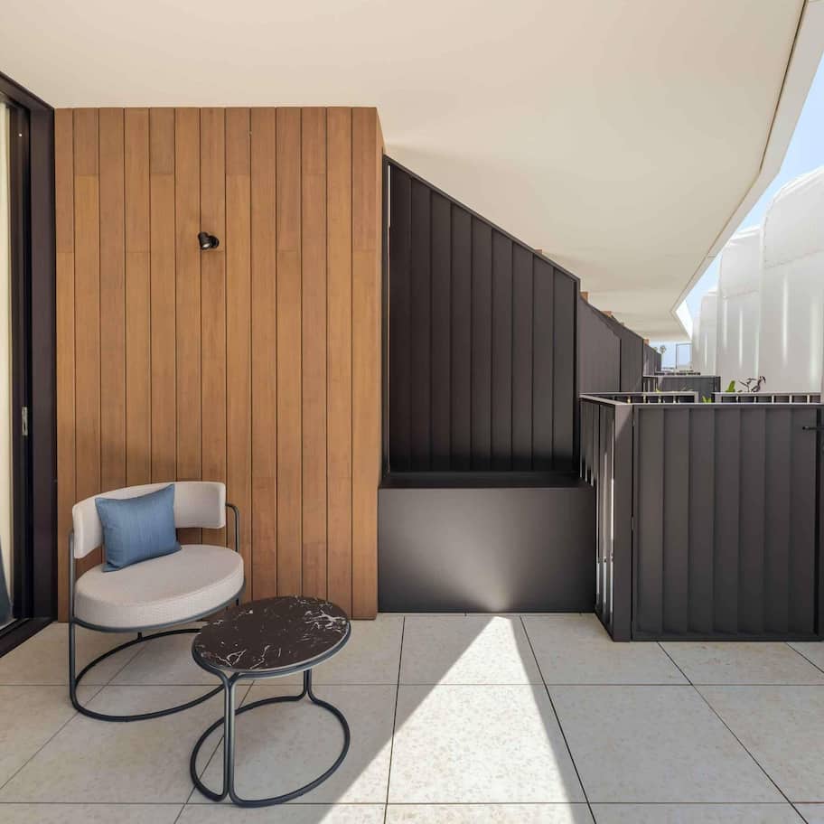 A modern balcony with a wooden panel wall, a round table with a chair, and a metal railing.