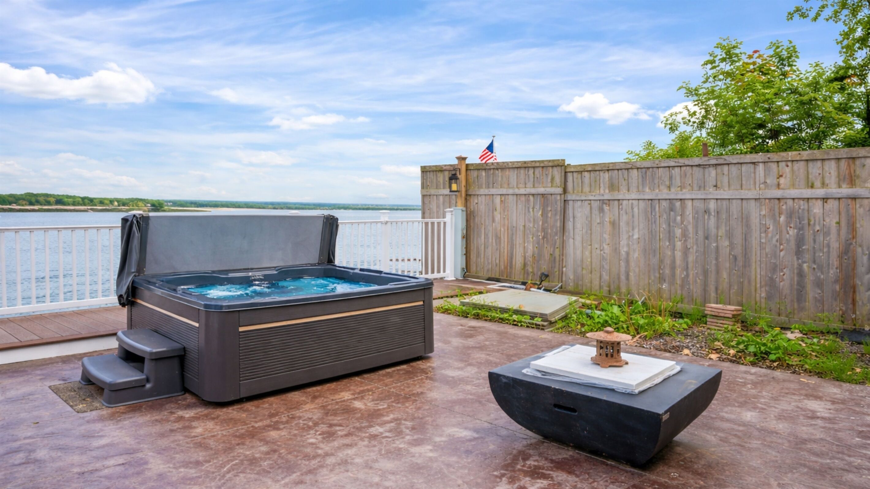 A hot tub on a deck with a view of a body of water and a wooden fence.
