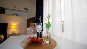 A hotel room with a dining table set with a bottle of wine, two wine glasses, a vase with a single white flower, and a bowl of strawberries. - Modern Studio apartment "Zara" with private balcony, shared pool (Pula)