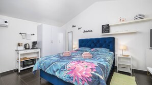 A modern bedroom with a large bed, a built-in wardrobe, a small kitchenette, and a wall-mounted shelf with decorative items. - Modern Studio apartment "Zara" with private balcony, shared pool (Pula)