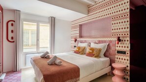 Ein Schlafzimmer mit einem Bett, einem Fenster, einem pinken Hocker und Wandfliesen mit Muster.