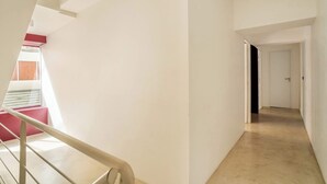 Ein Flur mit Treppe, einer Tür am Ende und einem Fenster mit Jalousien.