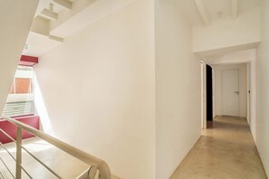 A hallway with a staircase, a door at the end, and a window with blinds. - Les Halles - Luxurious & colorful 5BD for 16 guest (Paris)