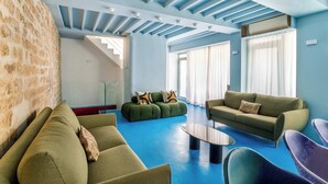 Ein modernes Wohnzimmer mit blauem Boden, grünen Sofas, einem Couchtisch und einer Treppe, die zu einer oberen Ebene führt.